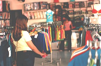 Moça vendo blusa no cabide de uma loja de roupas 